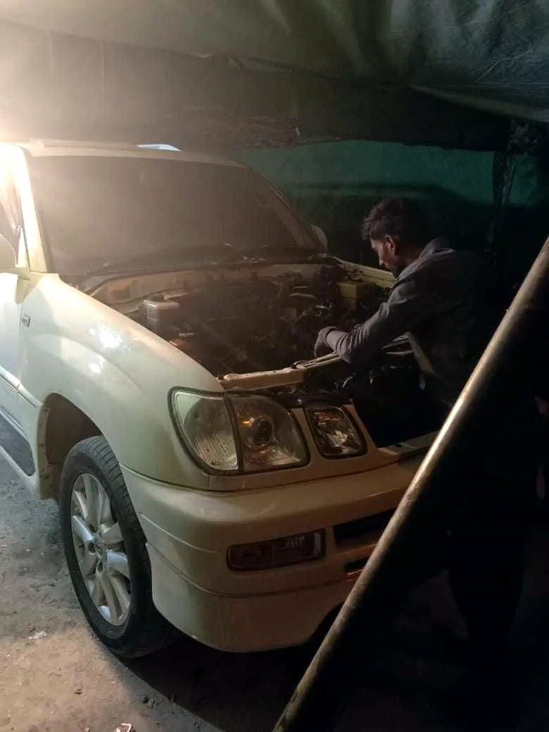 A Toyota Land Cruiser with its bonnet open, being worked on at night